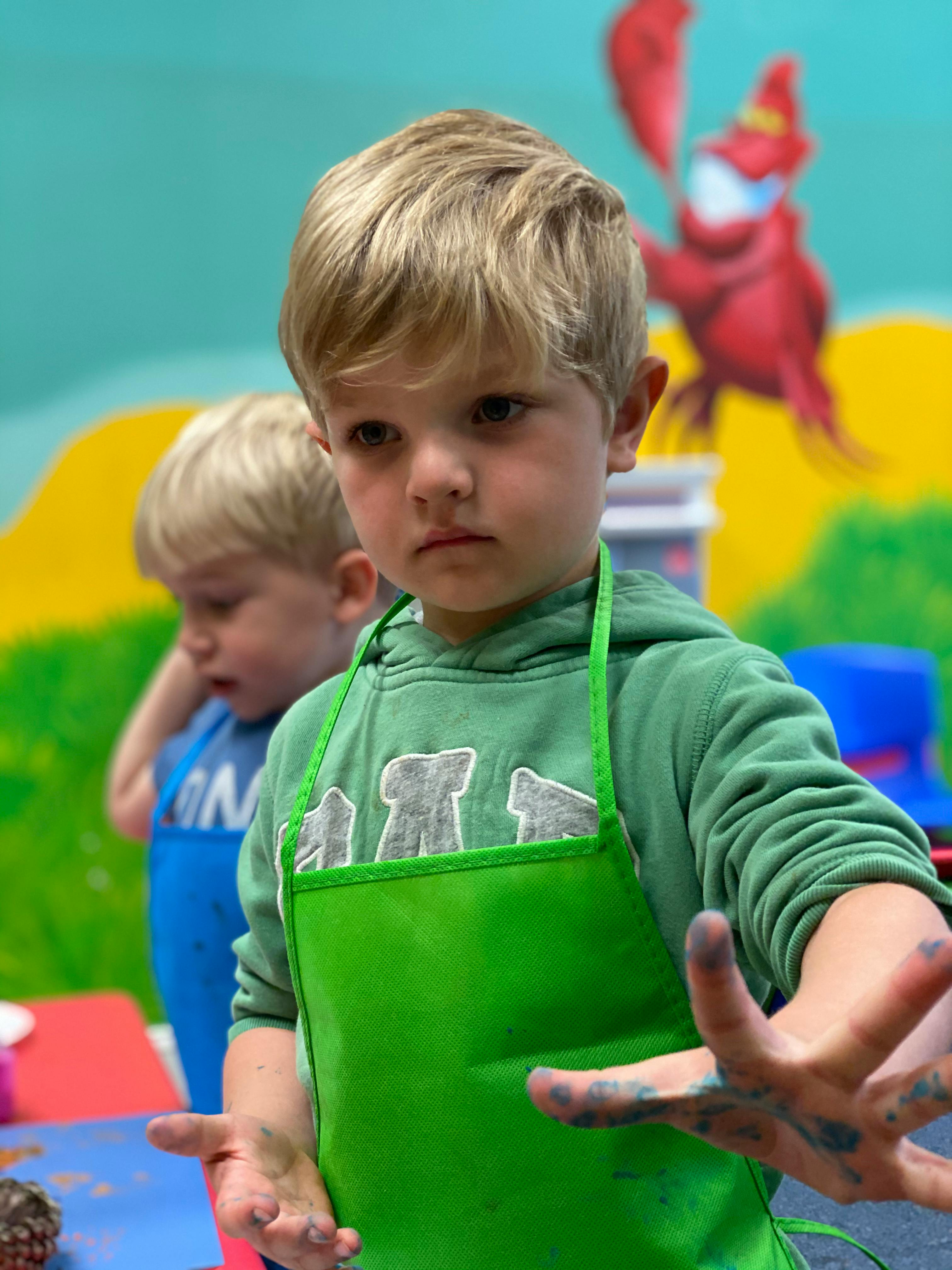 Child in green apron with paint on hands