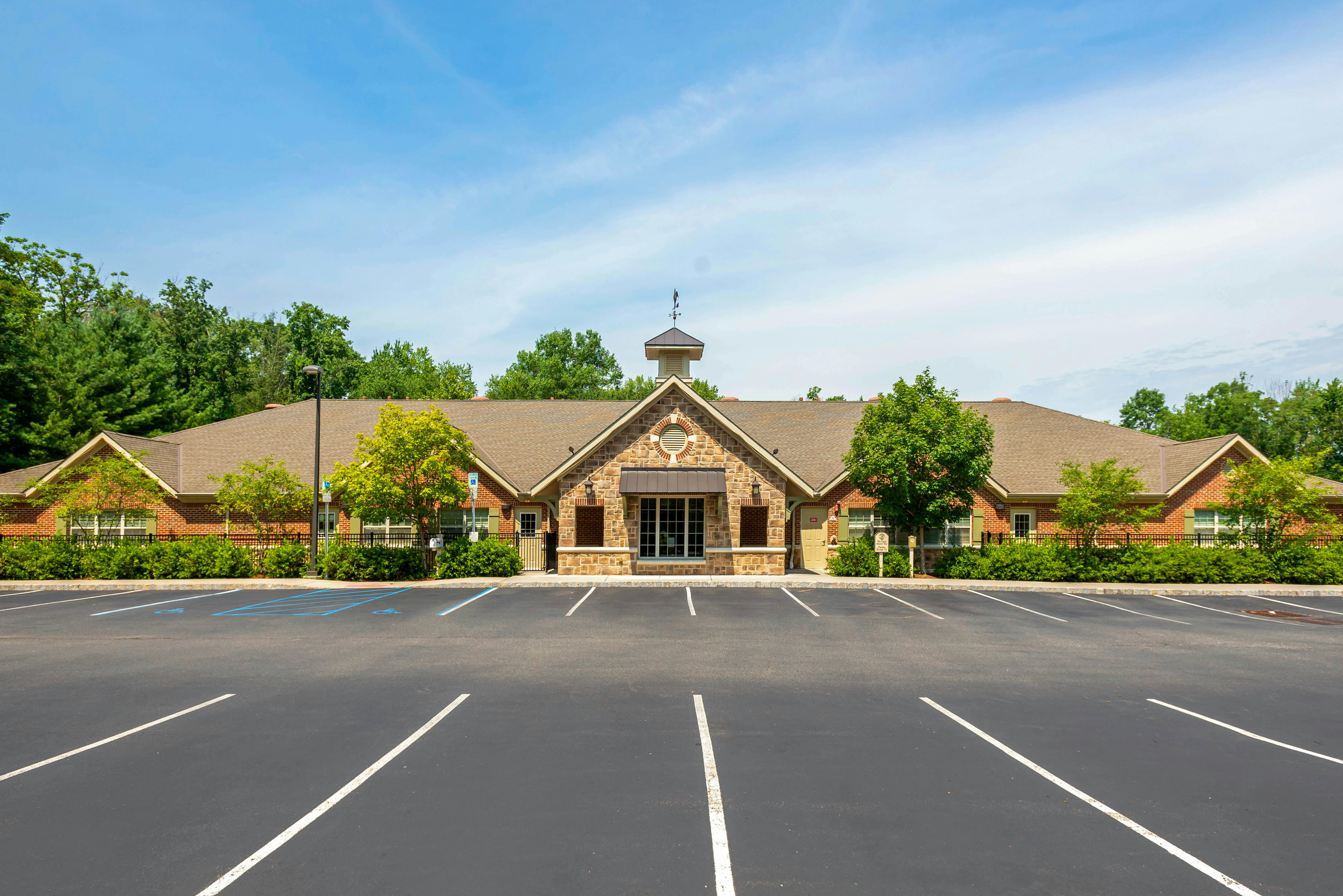 Brick and stone building with a parking lot and trees under a blue sky