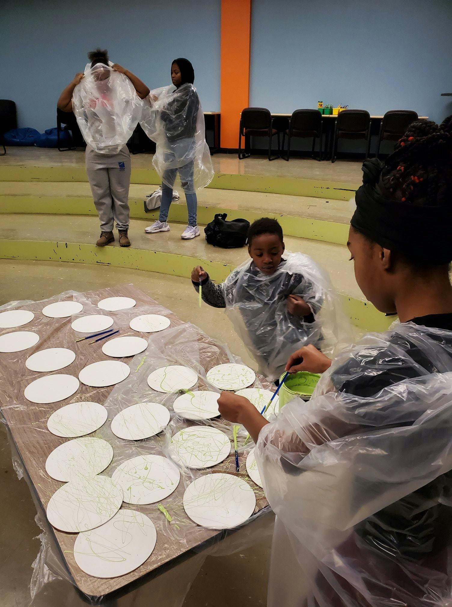 People wearing plastic ponchos painting white circular objects