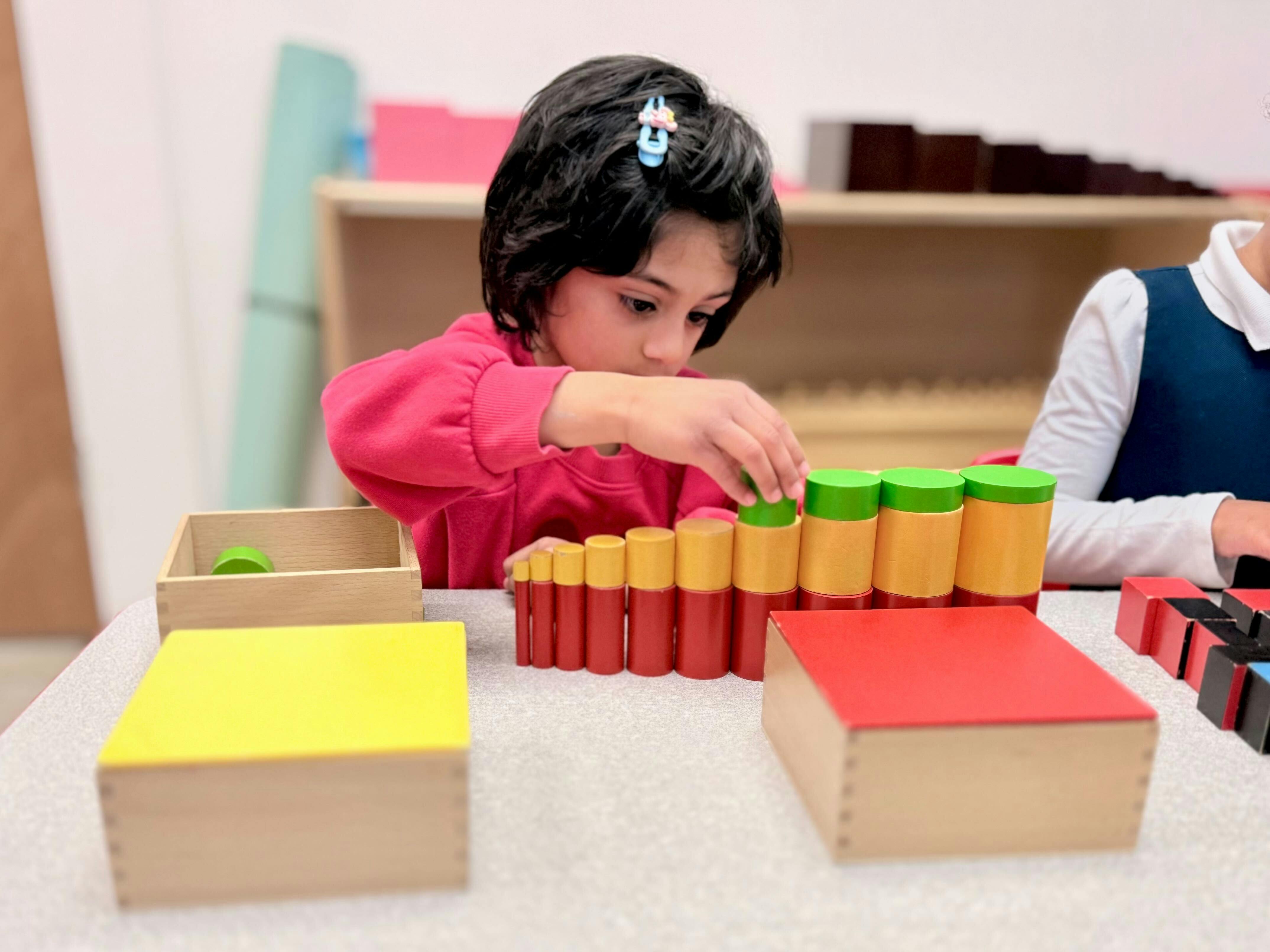 Child playing with wooden cylinder blocks in a classroom