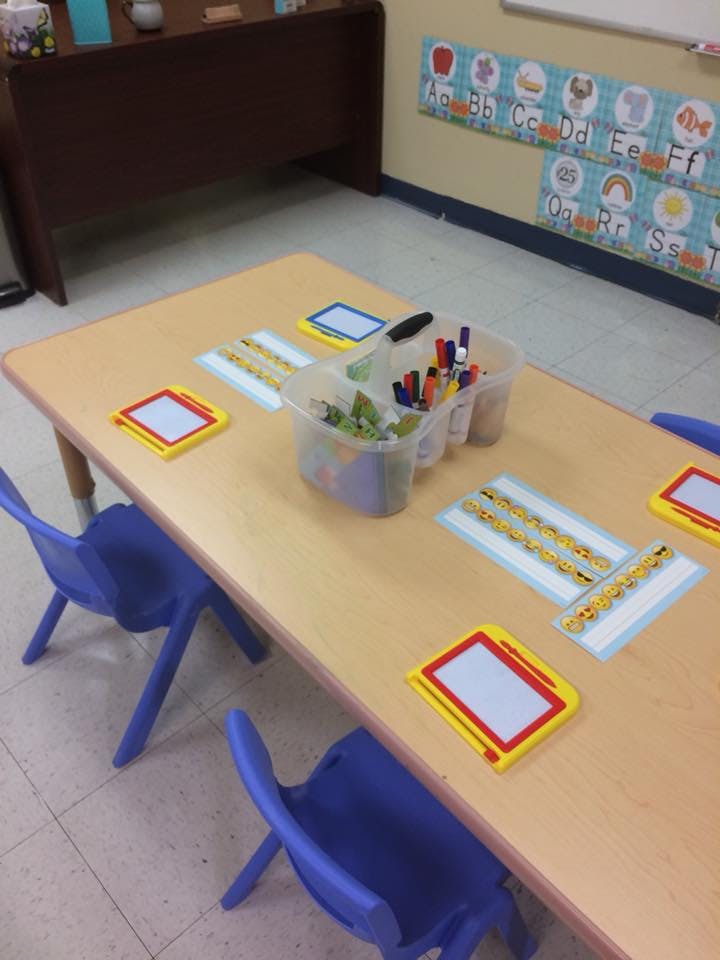 Classroom table with blue chairs, writing boards, and containers of markers