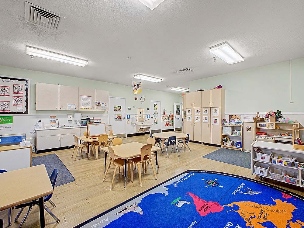 Classroom with child-sized tables and chairs, and a large world map rug