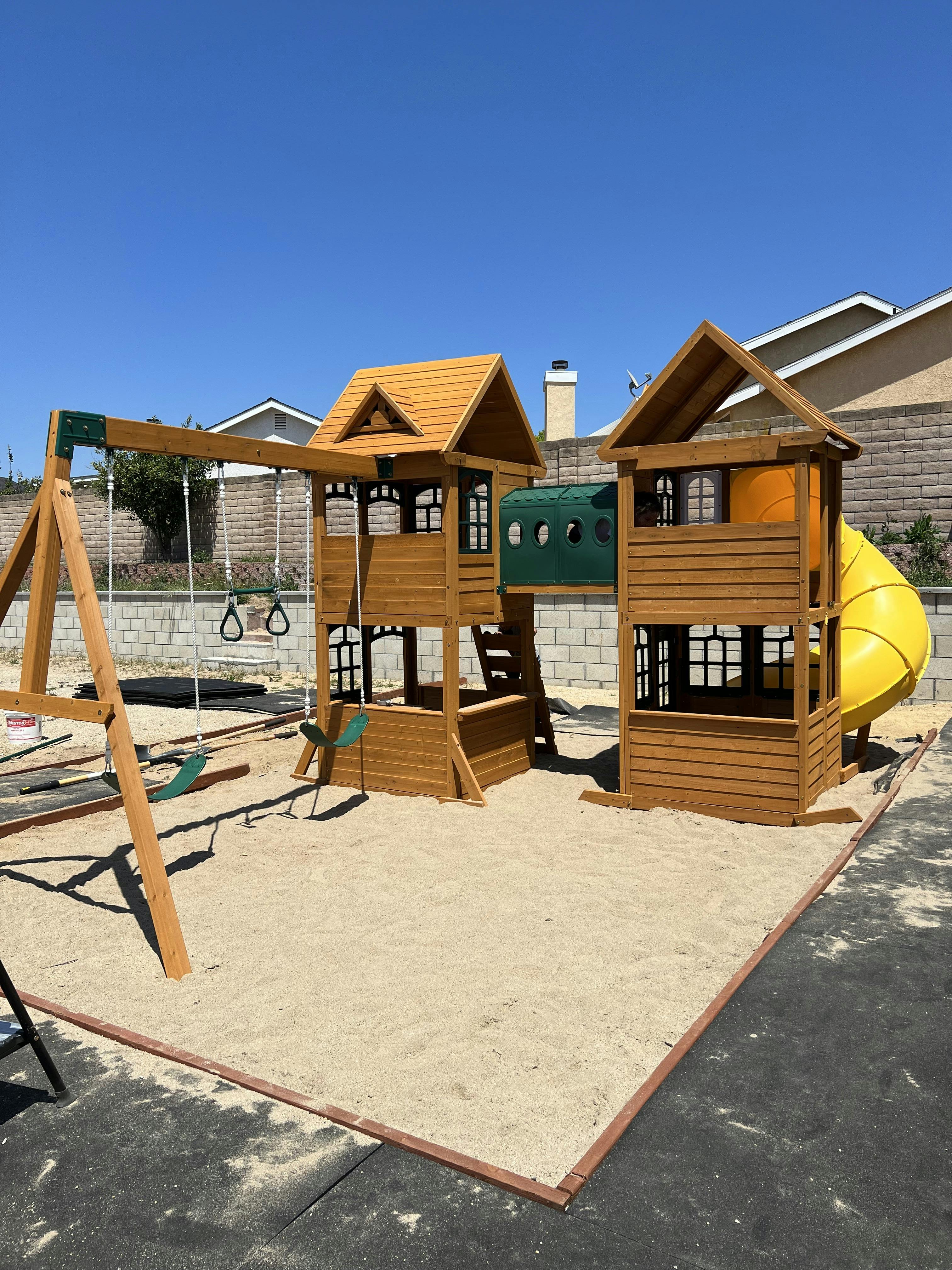 Wooden playground set with swings, slides, and playhouses on sand