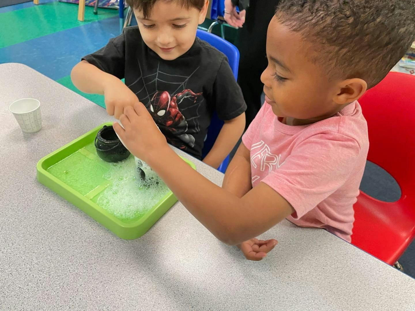 Two children playing with bubbles in a green tray on a table