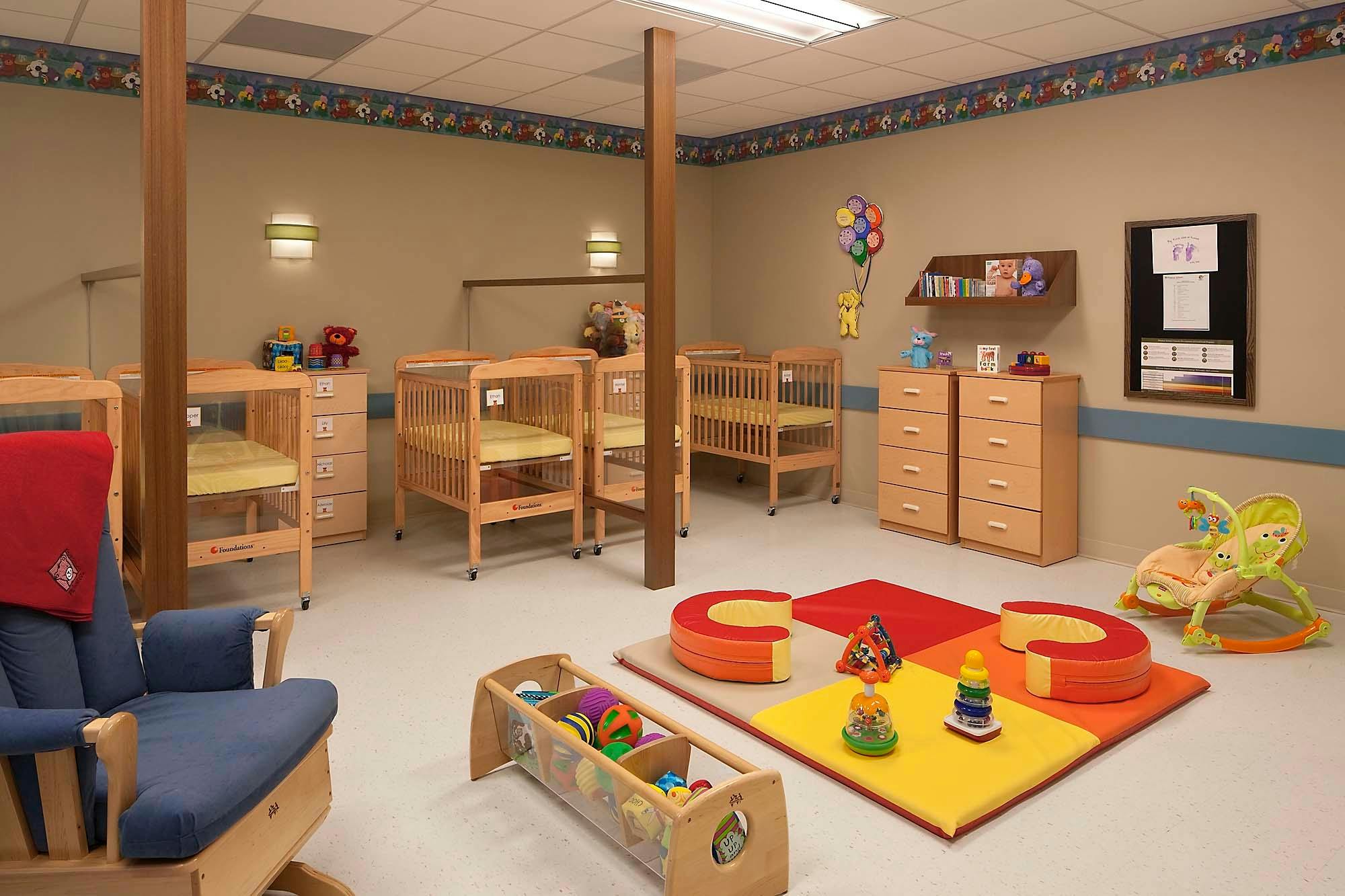 Nursery room with multiple cribs, a rocking chair, and play mats with soft blocks