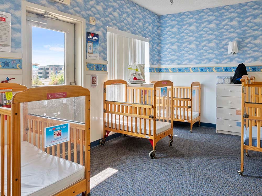 Several cribs in a room with cloud and moon wallpaper