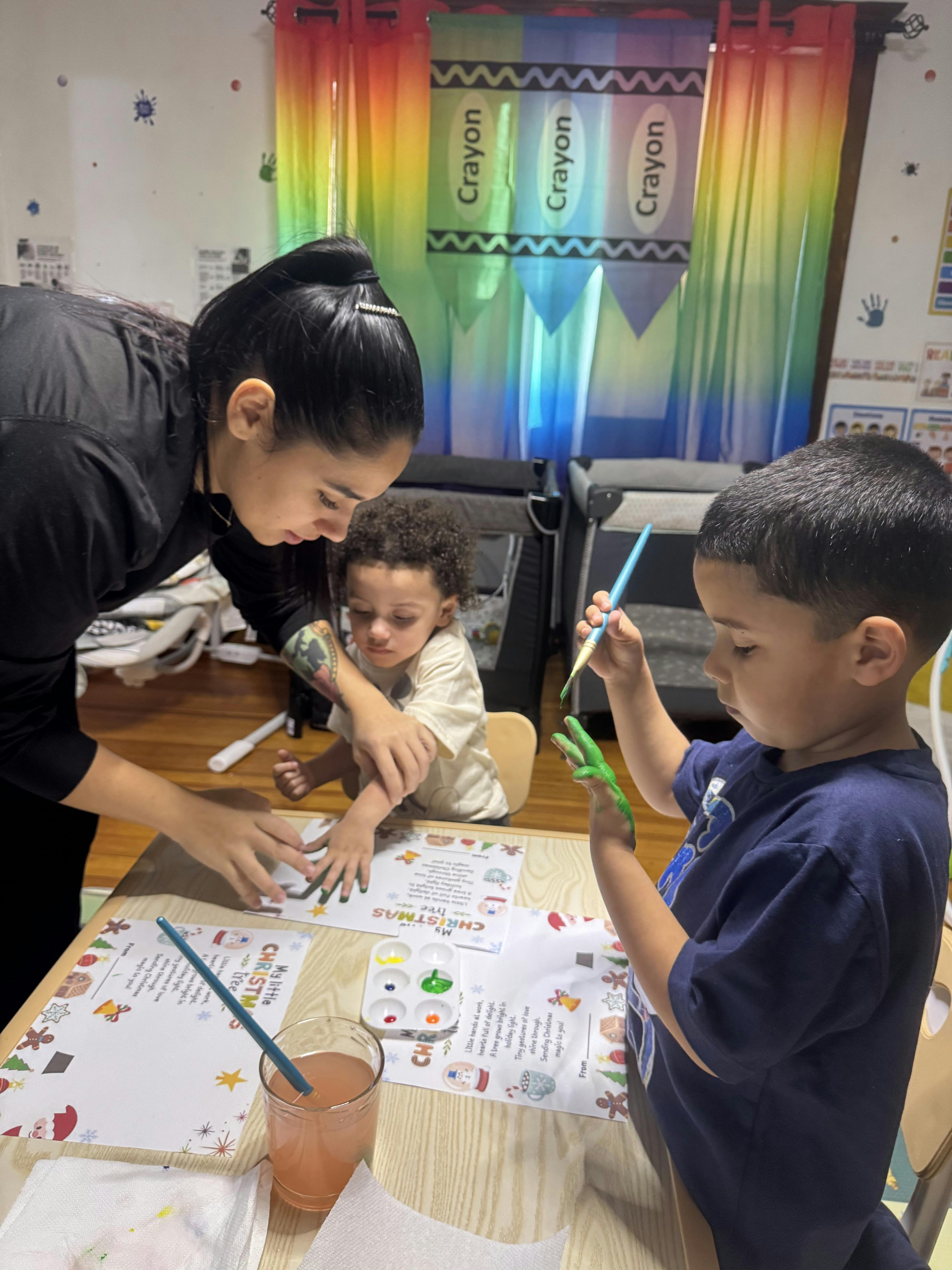person helping two children with green handprint painting in a classroom