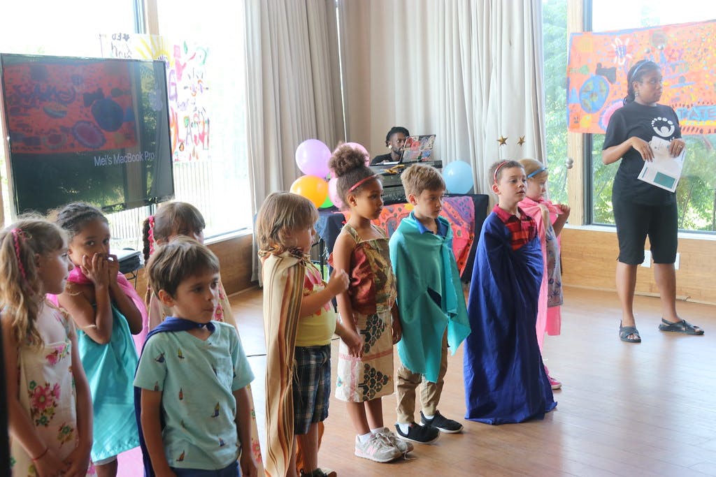 Children in costumes standing in a line with an adult in the background