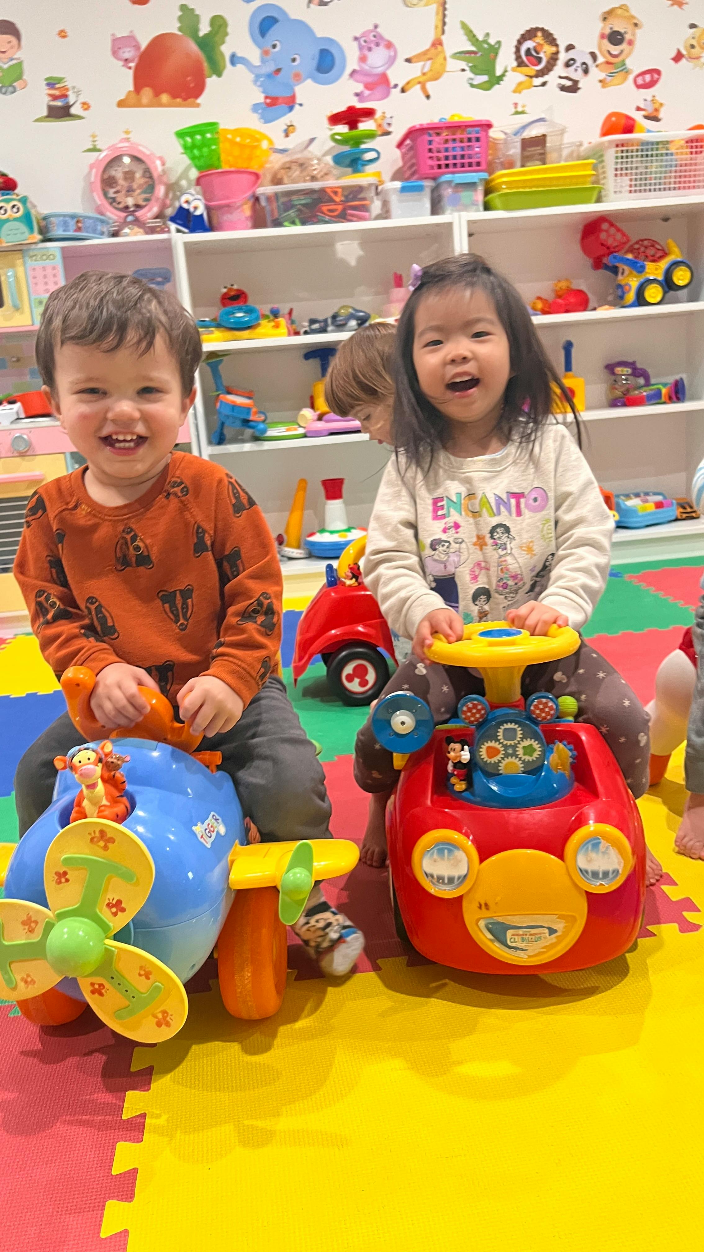 Two children playing with ride-on toys in a playroom