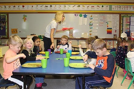 Adult serving food to children at a table in a classroom