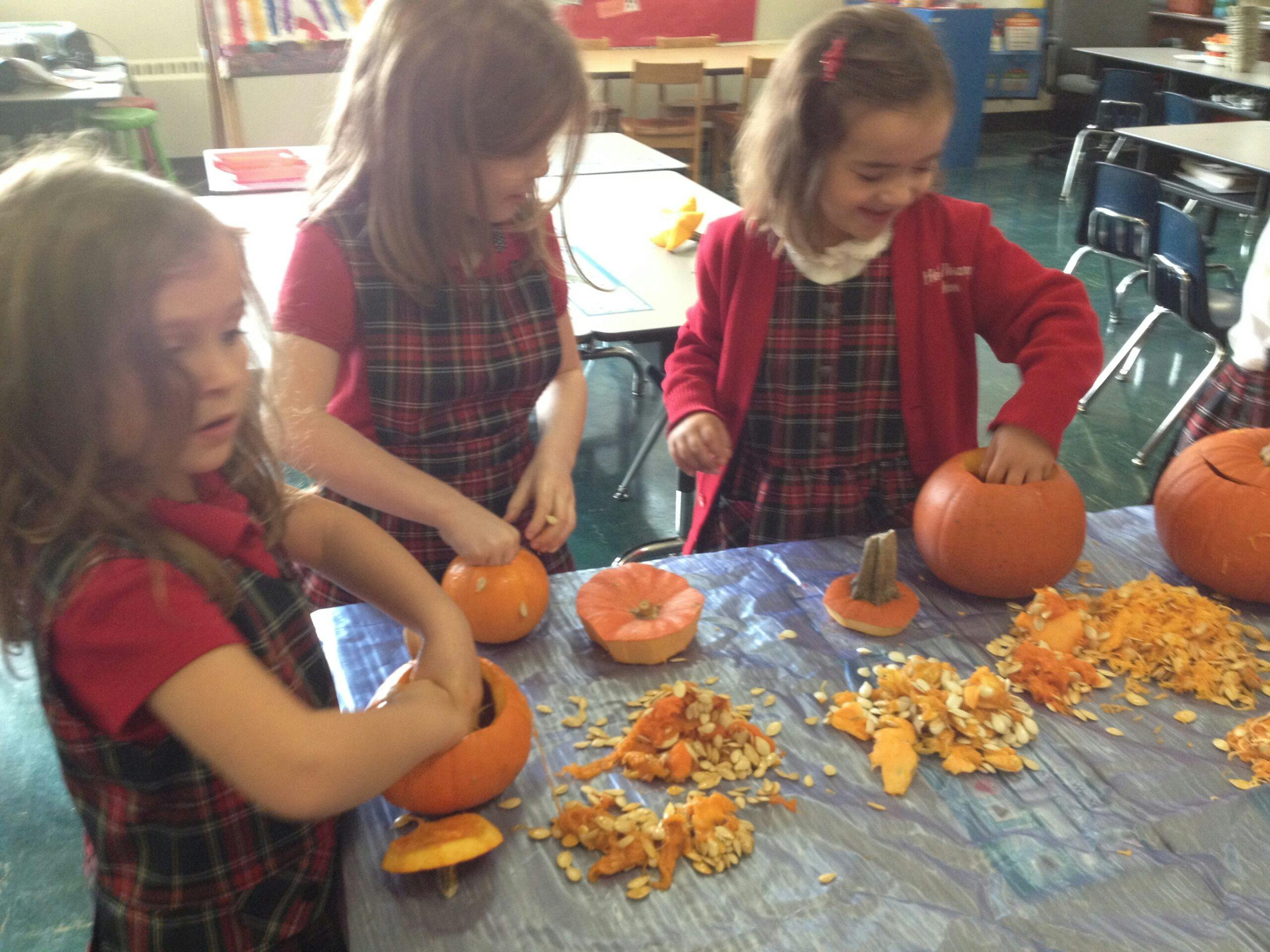 Three children in a classroom carving pumpkins