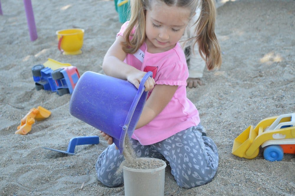 Child pouring sand from a purple bucket into a smaller bucket