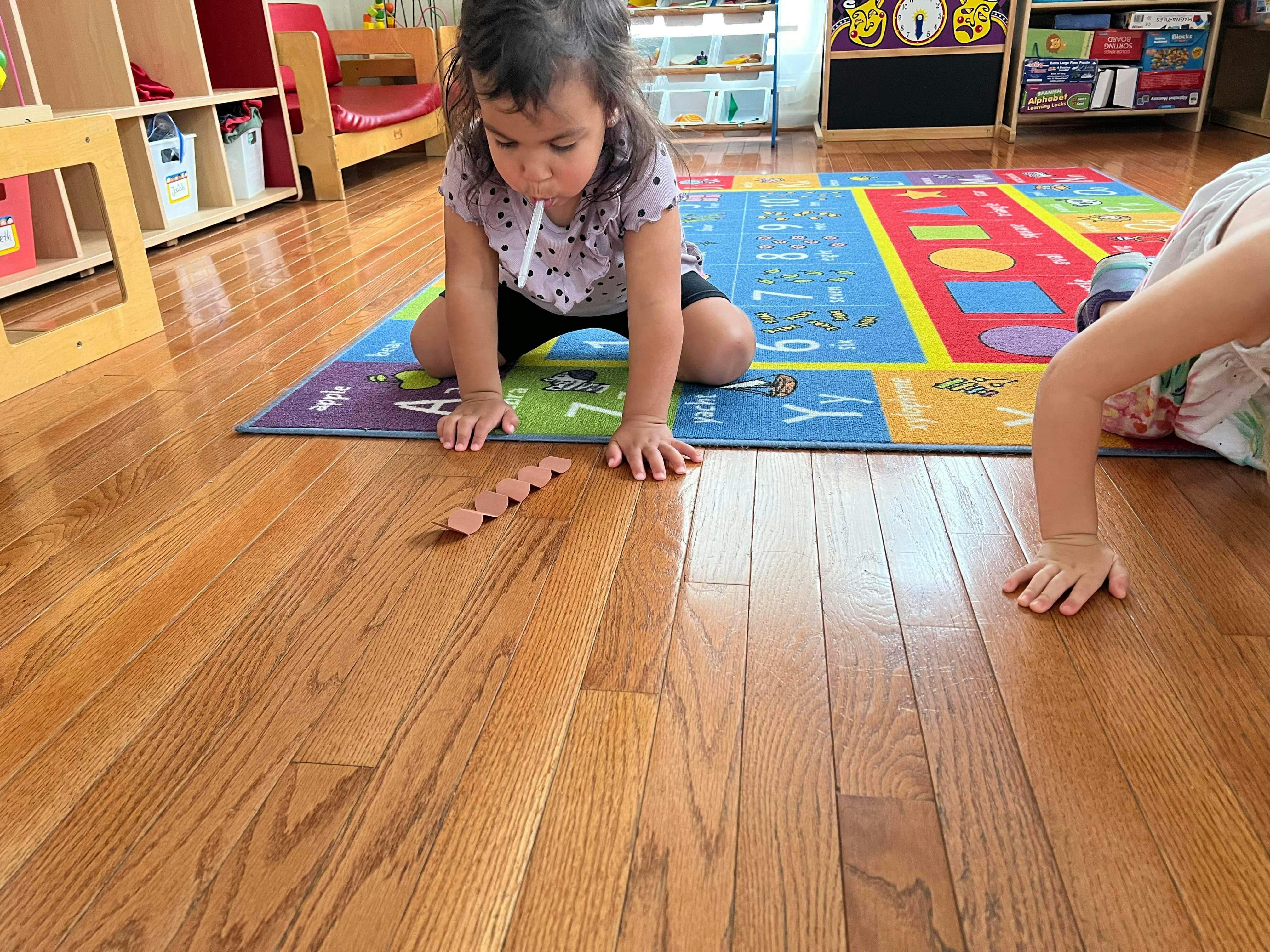 Child kneeling on a colorful rug, looking at a wooden puzzle piece on the floor