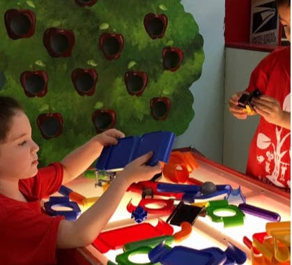 Child holding a blue object over a light table with colorful shapes
