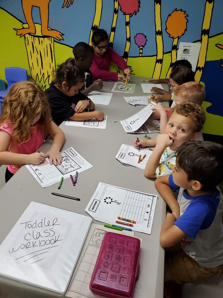 Children sitting at a table coloring and writing in a classroom