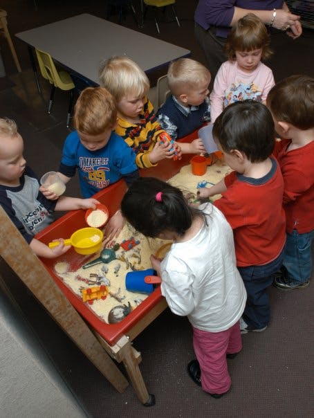 Children playing around a sand table with toys