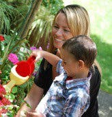 Person holding a child who is watering plants with a small watering can