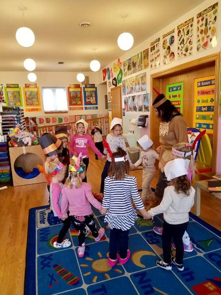 Children and an adult holding hands in a circle in a classroom