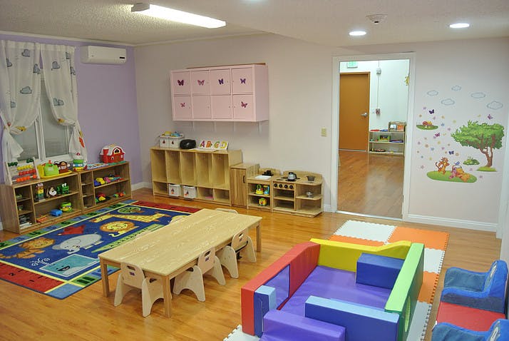 Playroom with small tables and chairs, shelves with toys, and colorful rugs