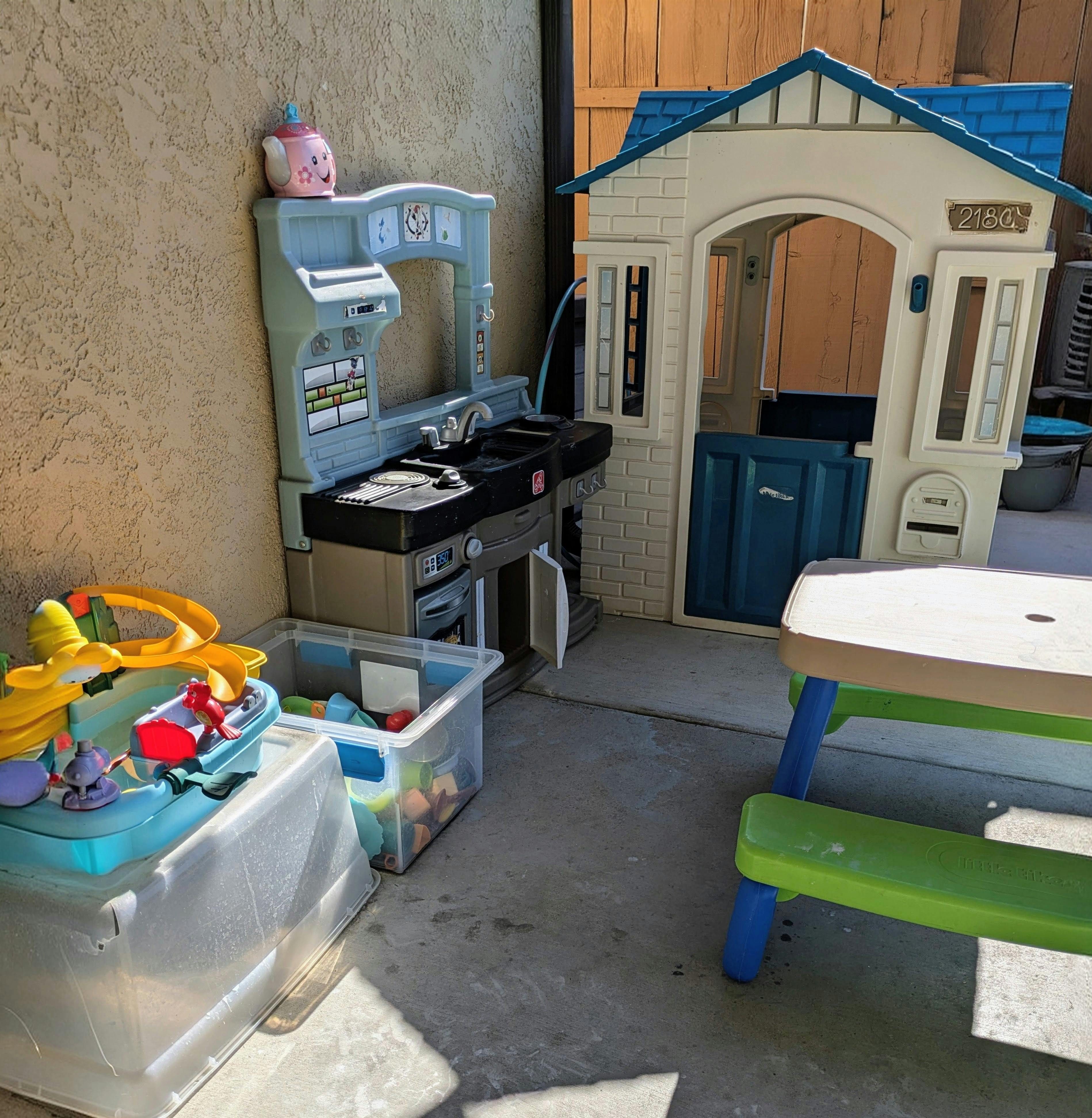 Outdoor play area with a toy kitchen, playhouse, and picnic table