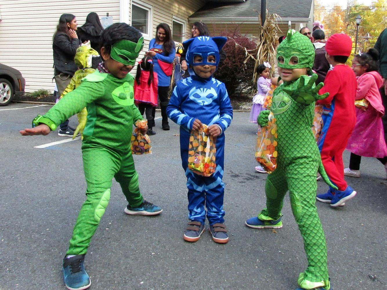 Three children in superhero costumes holding bags of candy