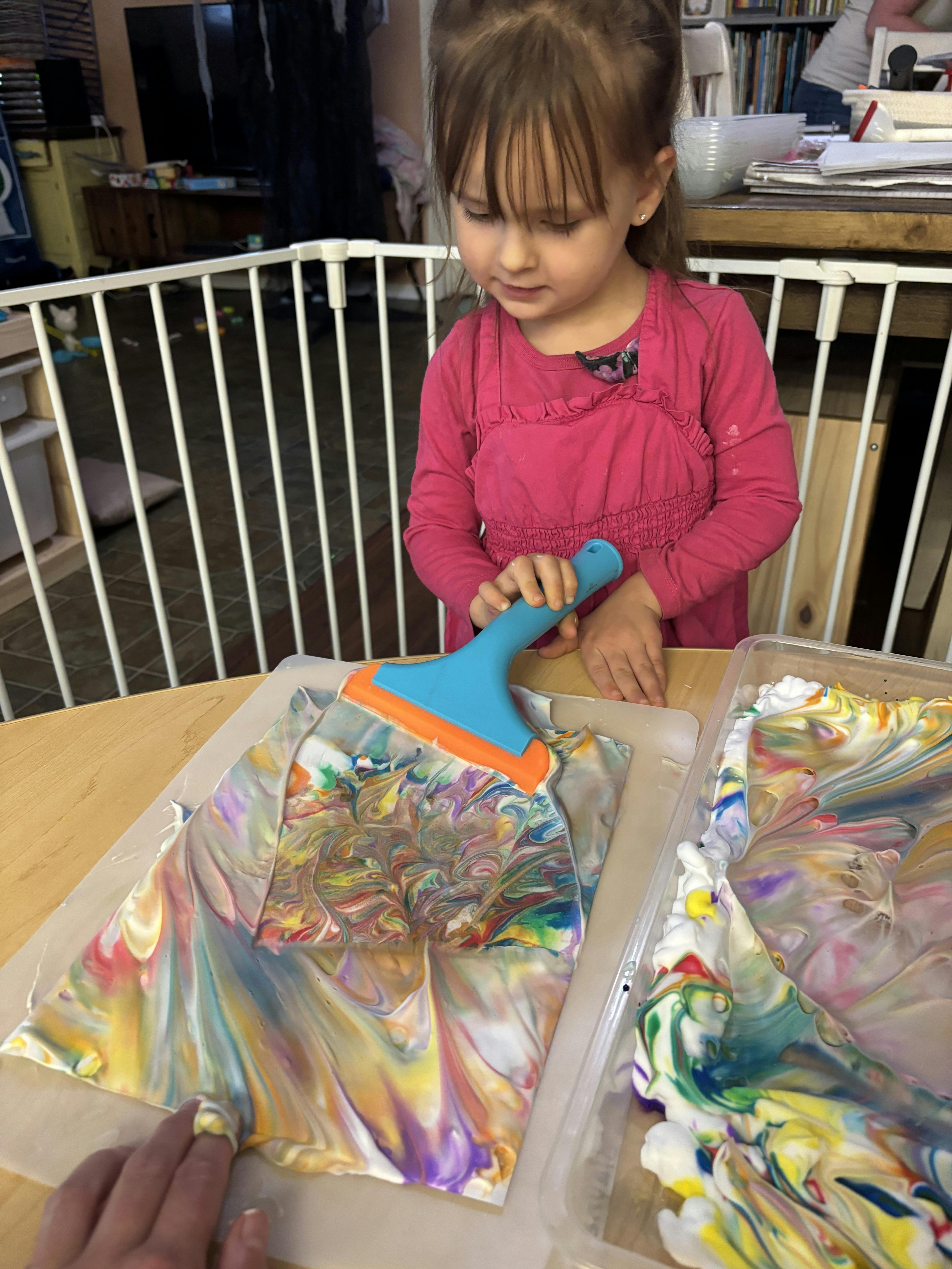 Child using a squeegee to spread colorful paint in a plastic bag