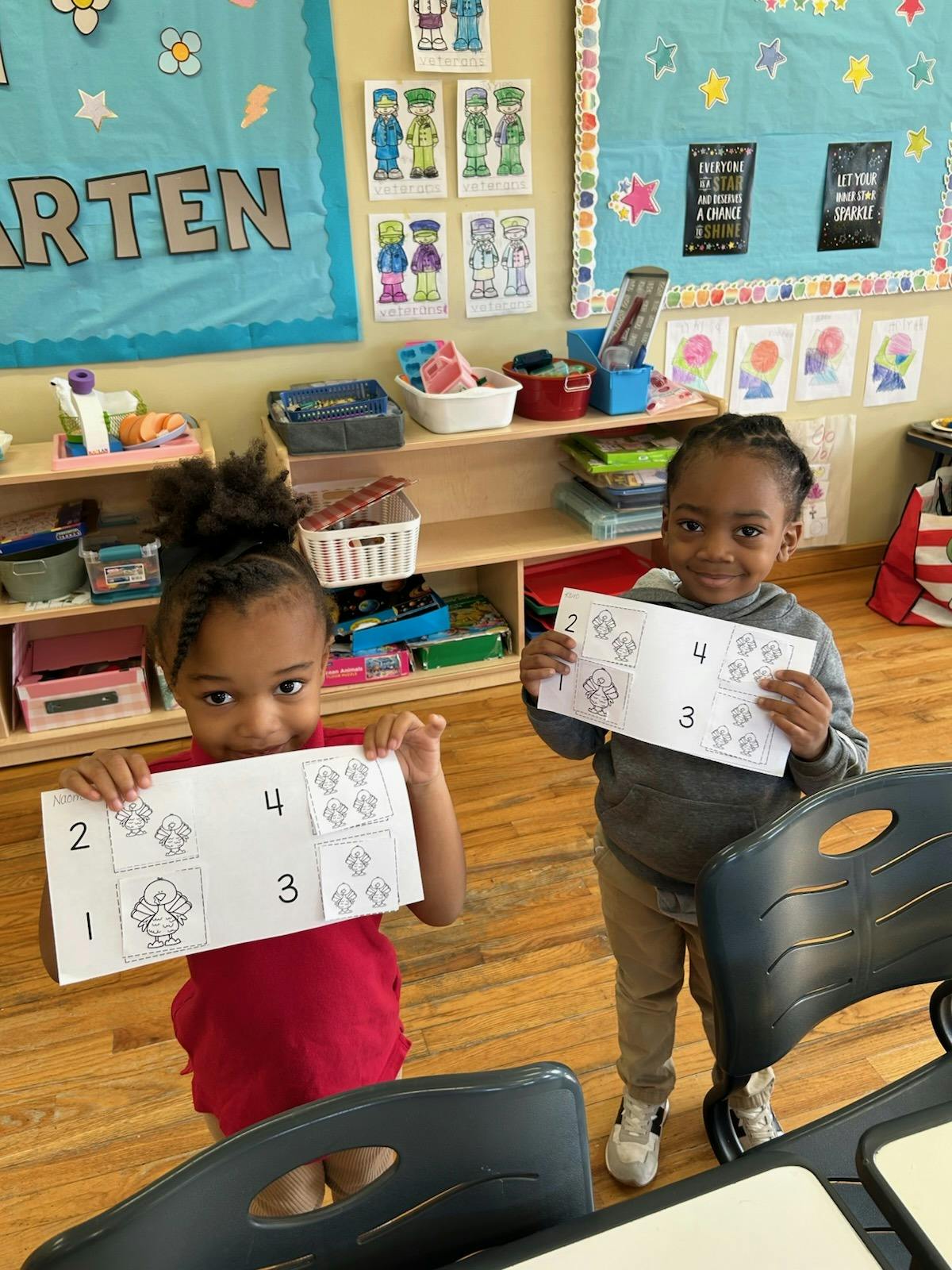 Two children holding up papers with numbers and pictures of turkeys in a classroom