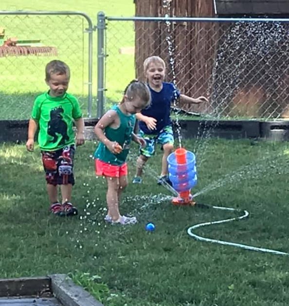Three children playing in water from a sprinkler