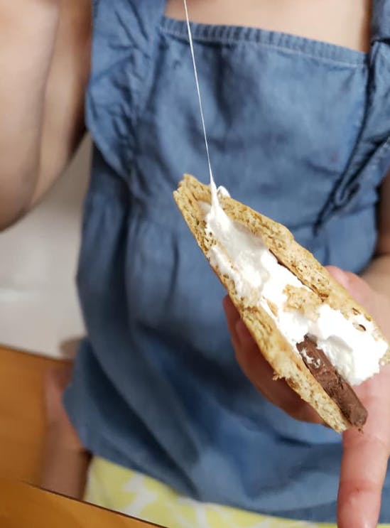Person holding a s'more with melted marshmallow stretching