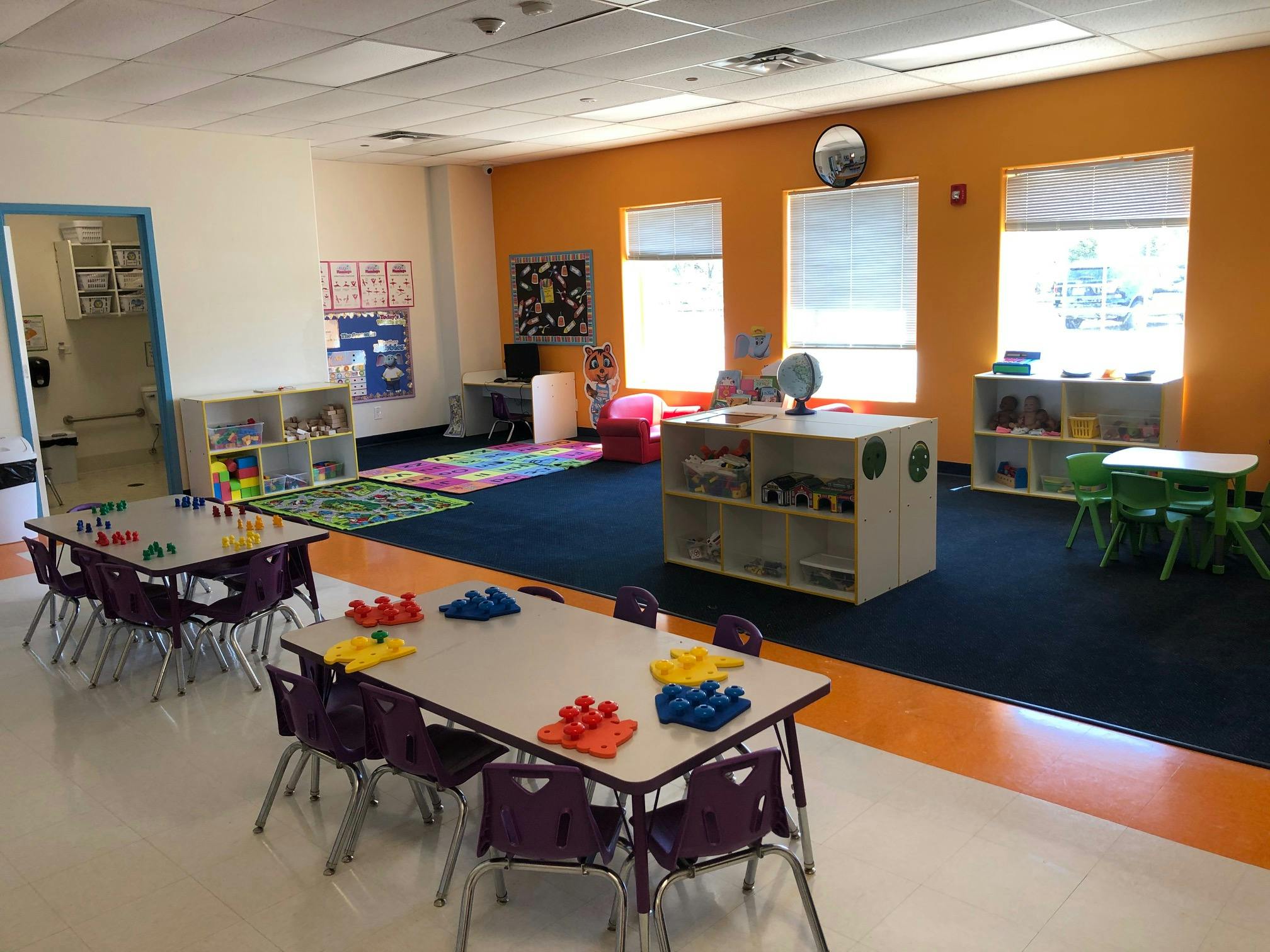 Classroom with small tables and chairs, colorful rug, and storage shelves