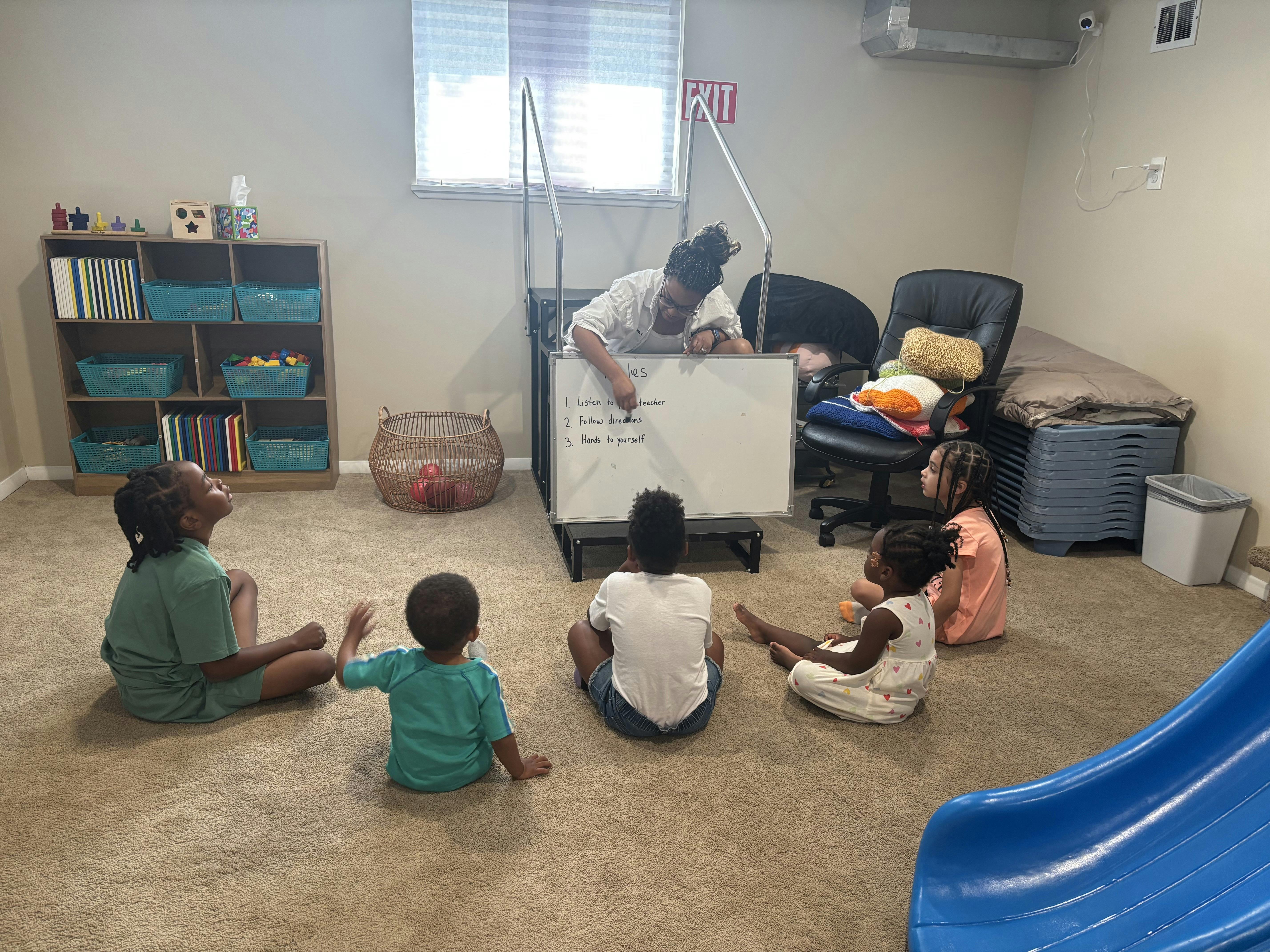 A person writing on a whiteboard for a group of children sitting on the floor