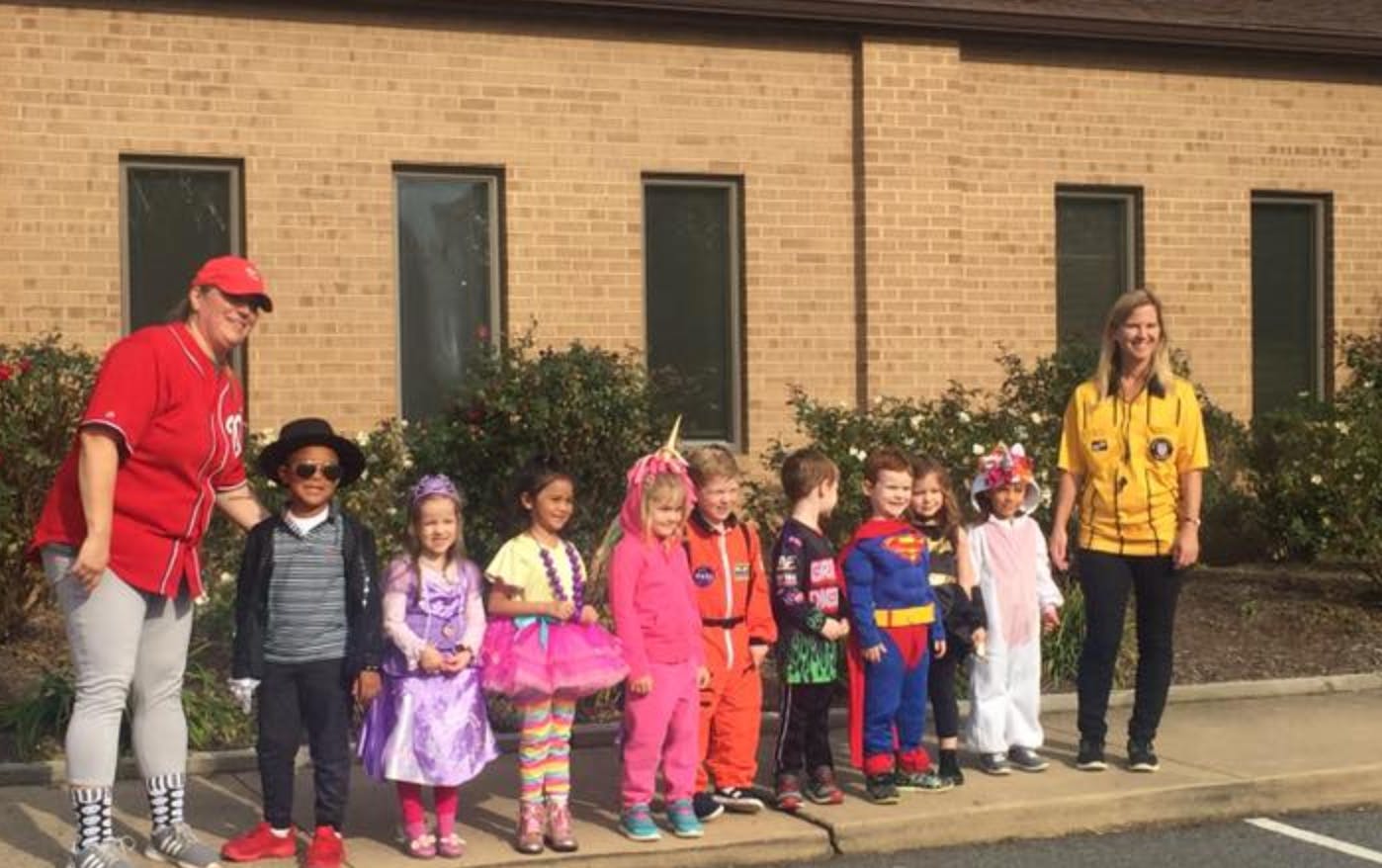 Two adults with a group of children in costumes standing in a line outdoors
