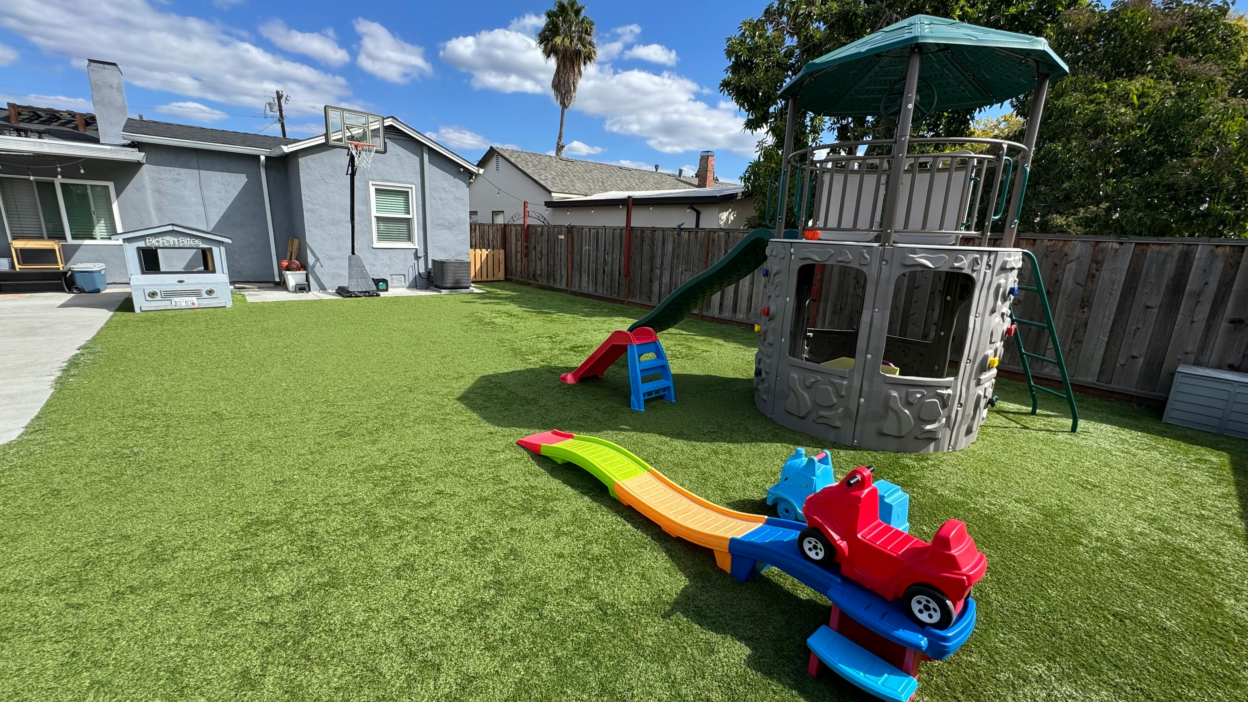 Backyard with artificial turf, play structure with slide, and a toy car roller coaster