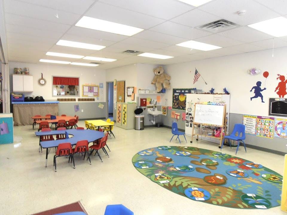 Empty classroom with small tables and chairs, and a colorful rug