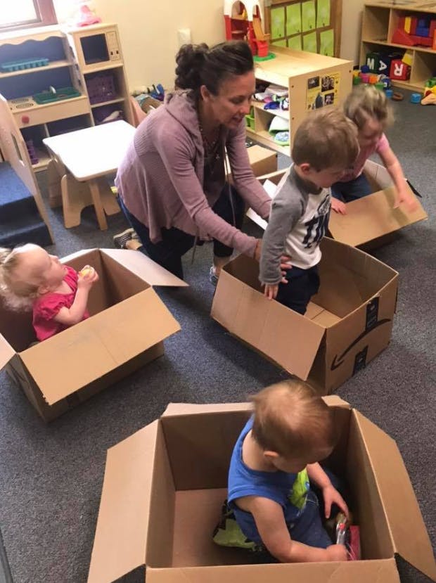Person helping children play with cardboard boxes in a classroom