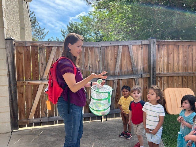 Adult holding a butterfly habitat while children watch