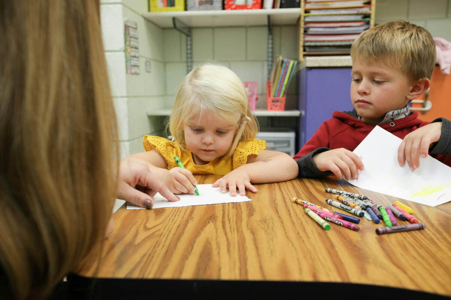 Two children drawing at a table with crayons