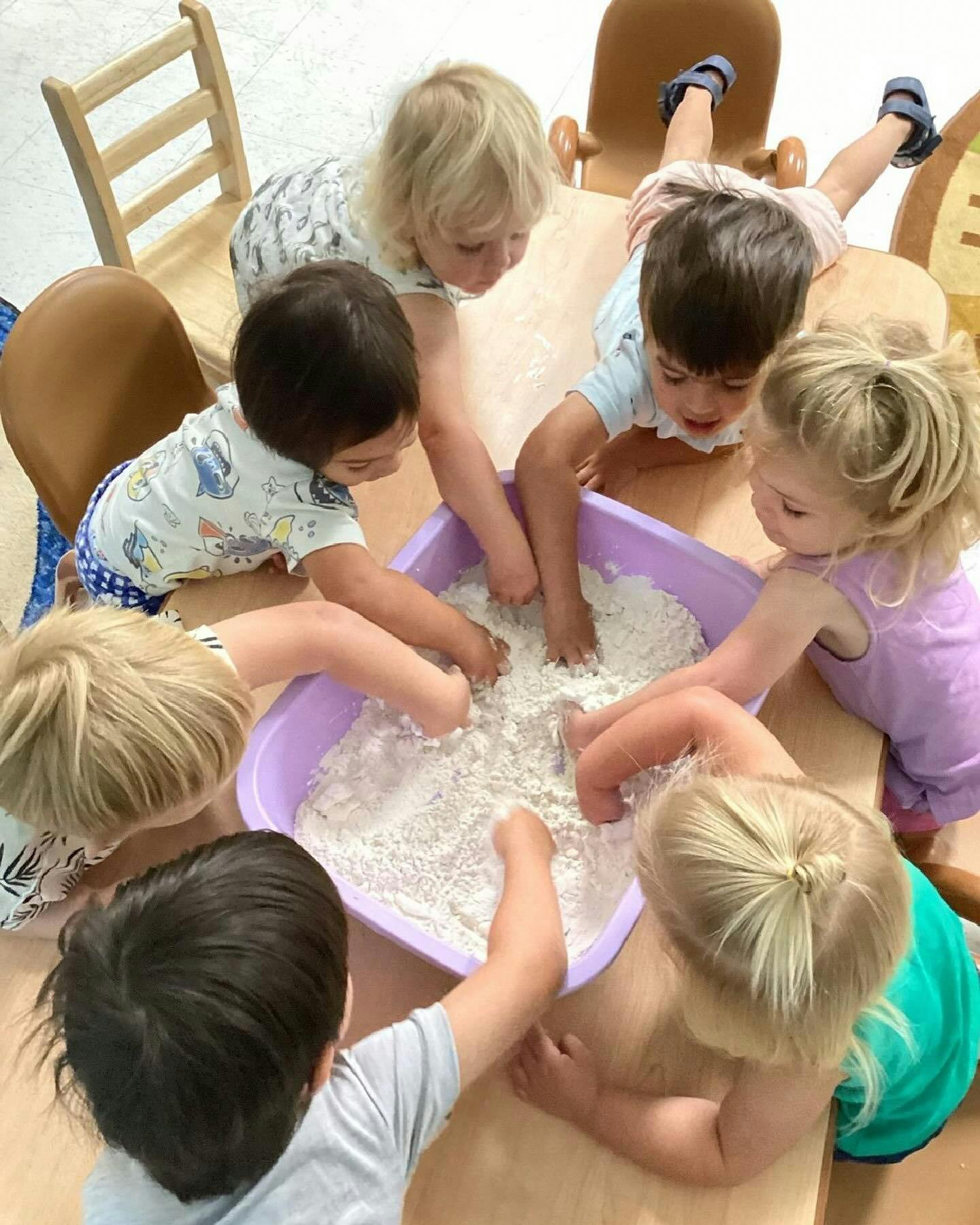 Children playing with flour in a purple bin on a table