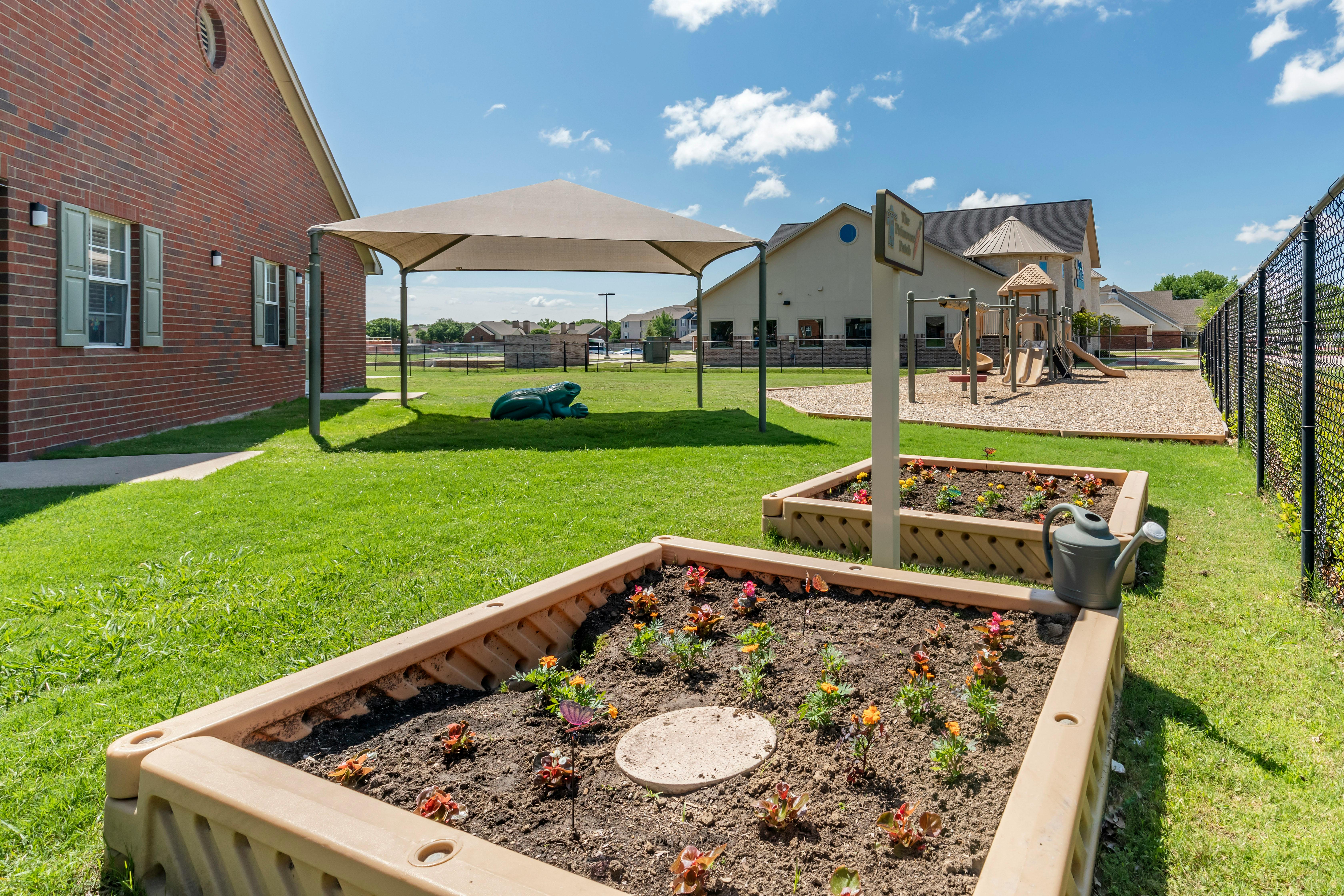Outdoor playground area with raised garden beds and brick building