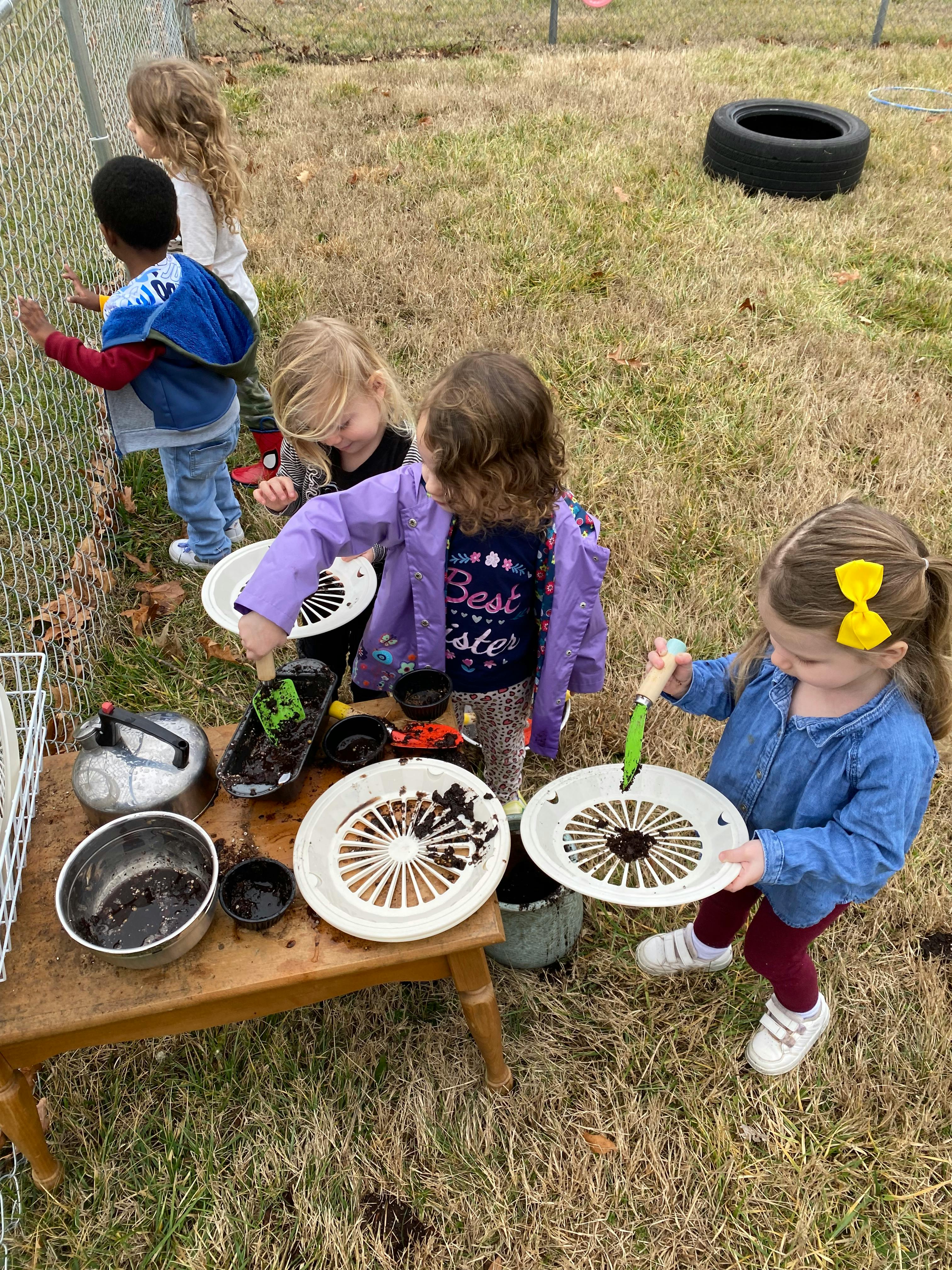 Children playing with dirt and kitchen items outdoors