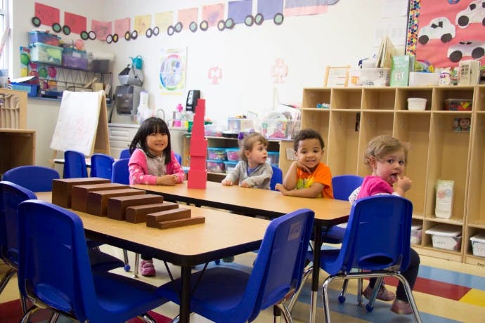 Four children sitting at tables in a classroom with wooden blocks