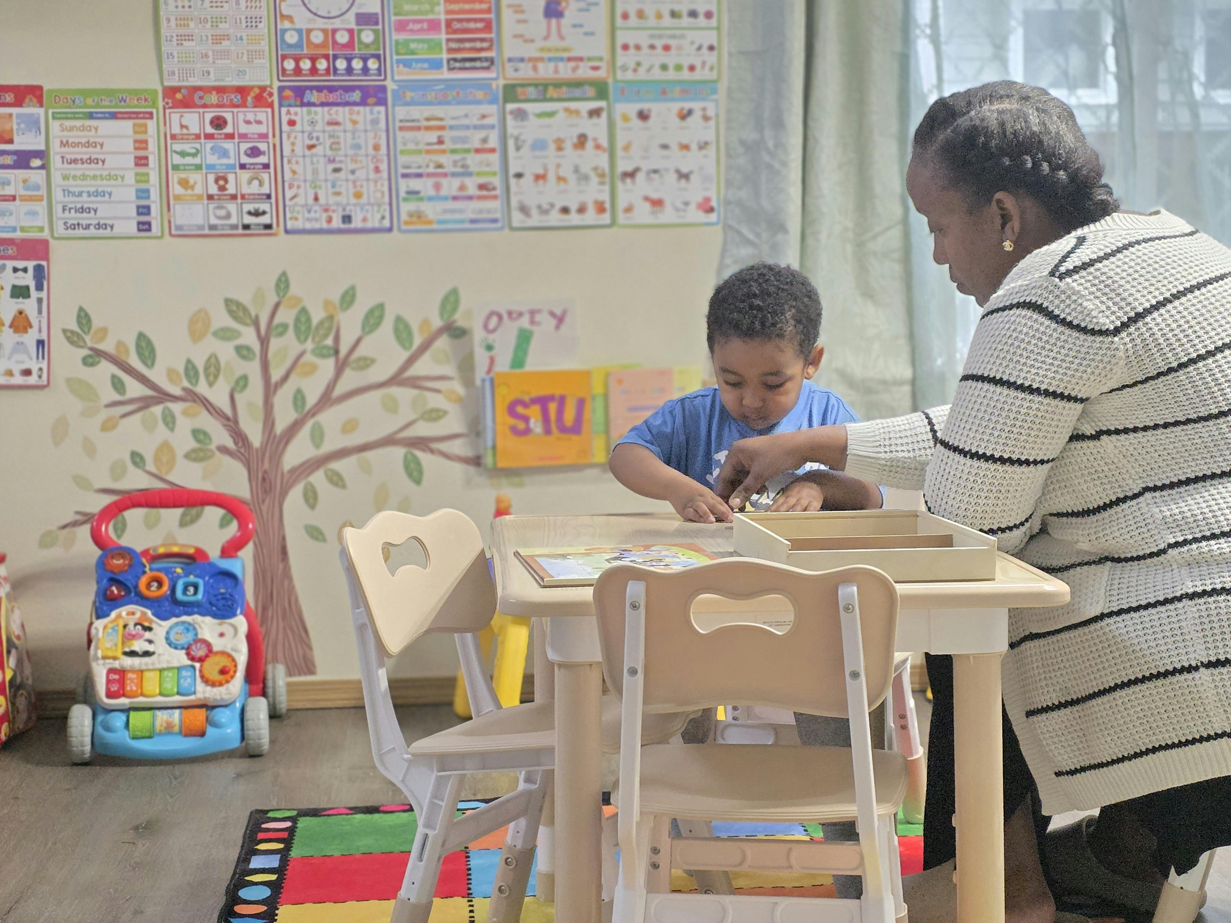 Adult and child seated at a small table, child playing with an object