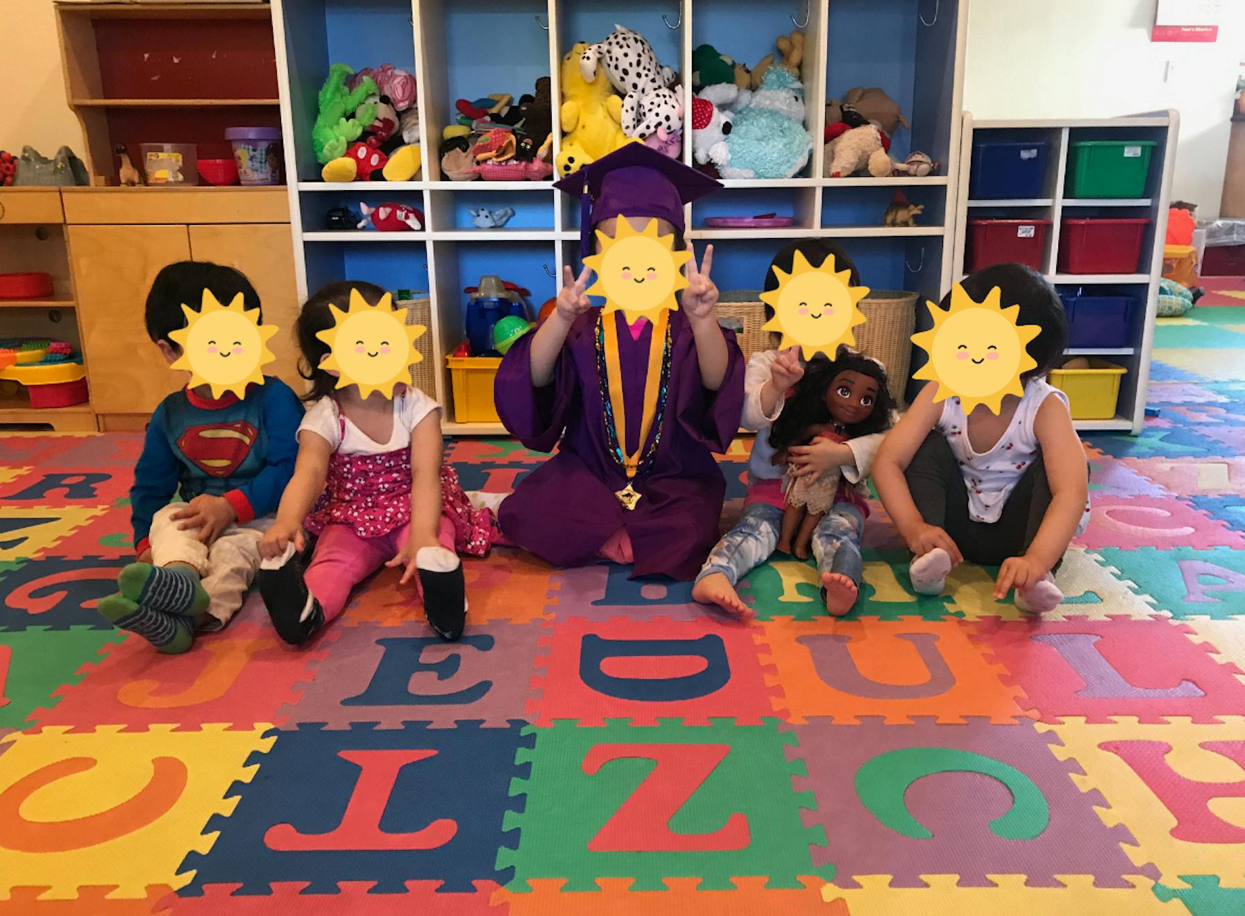 Group of children sitting on a play mat with one child wearing a graduation gown