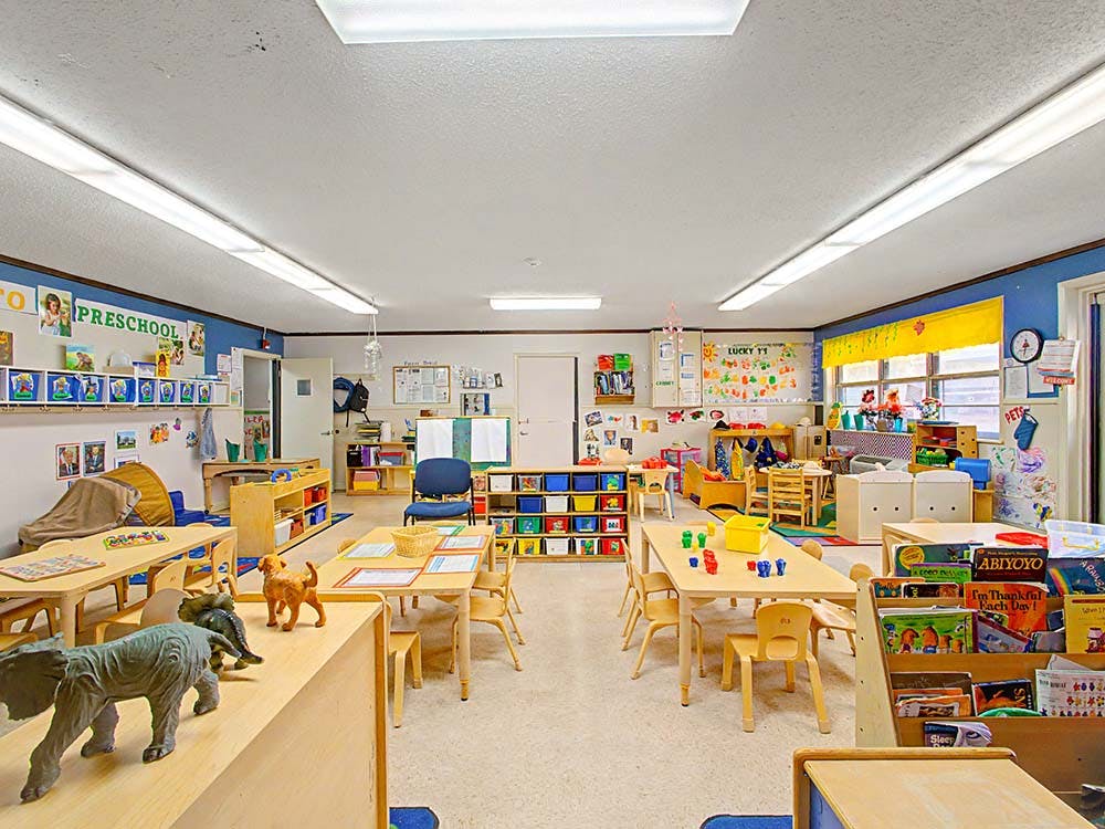 A colorful empty preschool classroom with small tables, chairs, and play areas