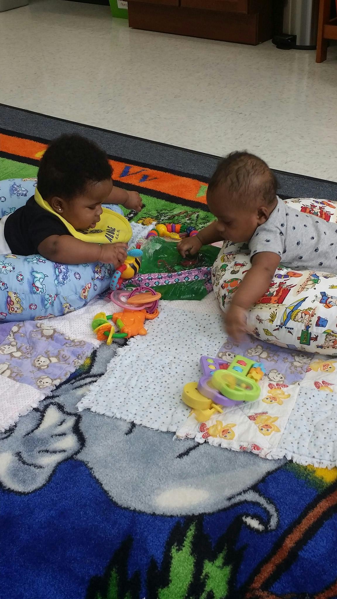 Two babies playing with toys on a colorful blanket