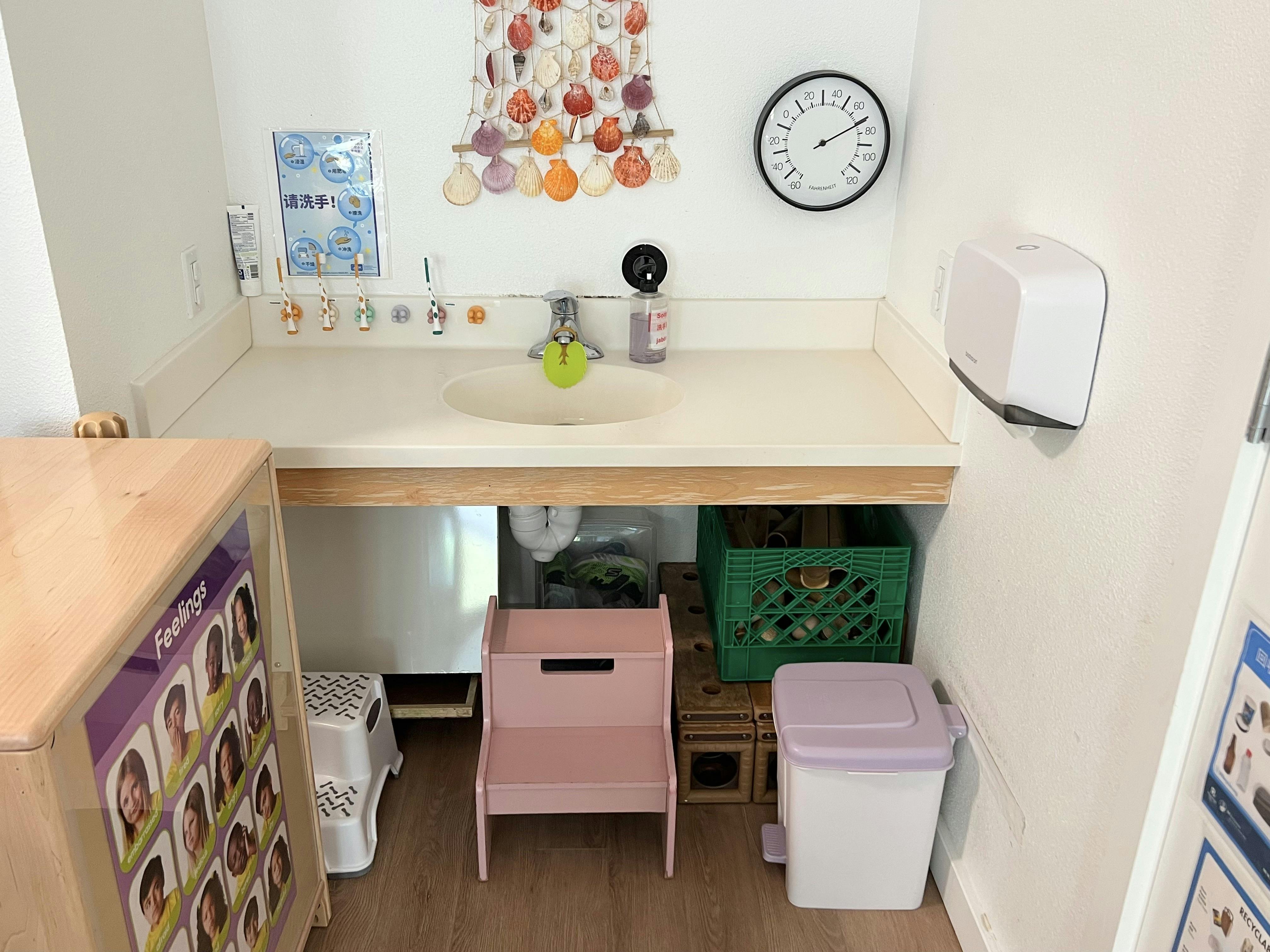 Child height sink with toothbrushes and step stools in a classroom setting