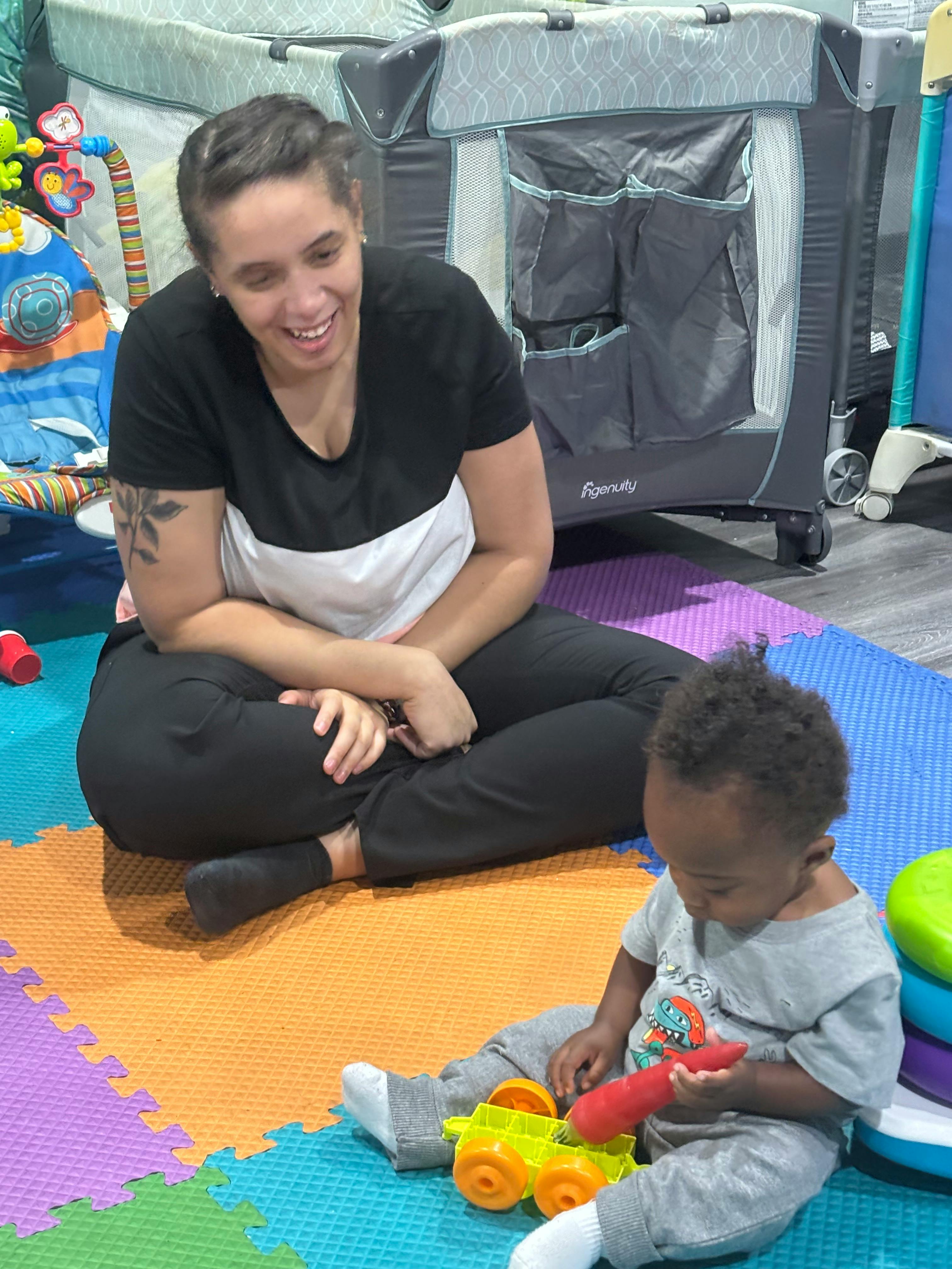 Person sitting on floor with child playing with toy truck