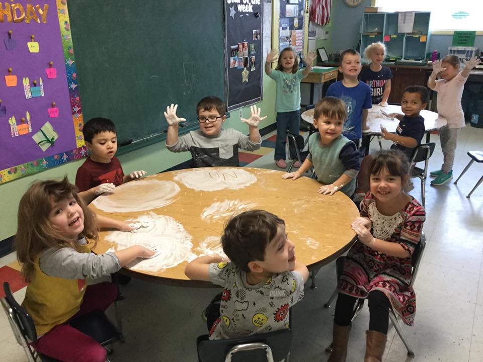 Children playing with flour on a table in a classroom