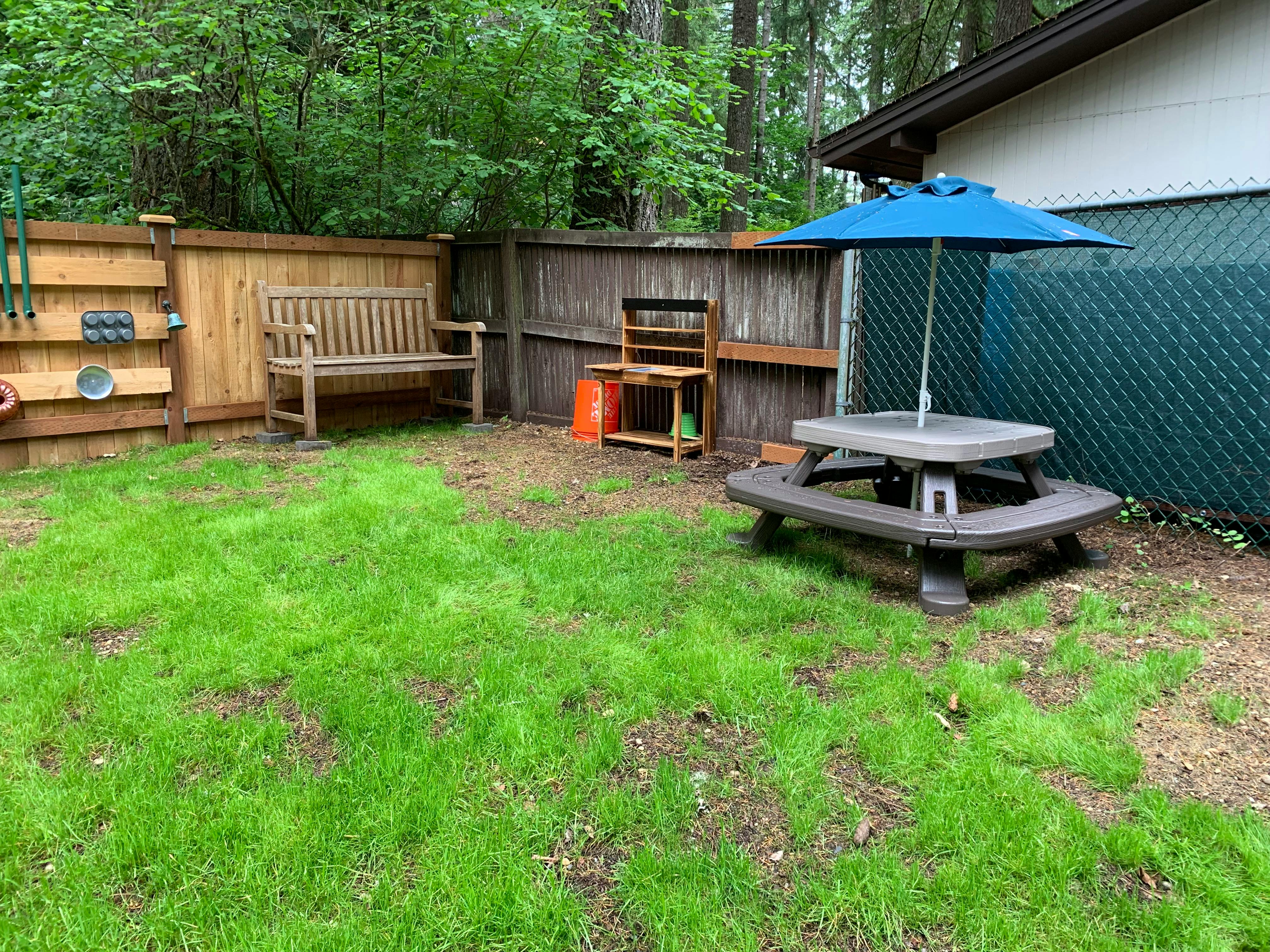 Backyard with a wooden bench, picnic table with umbrella, and green grass
