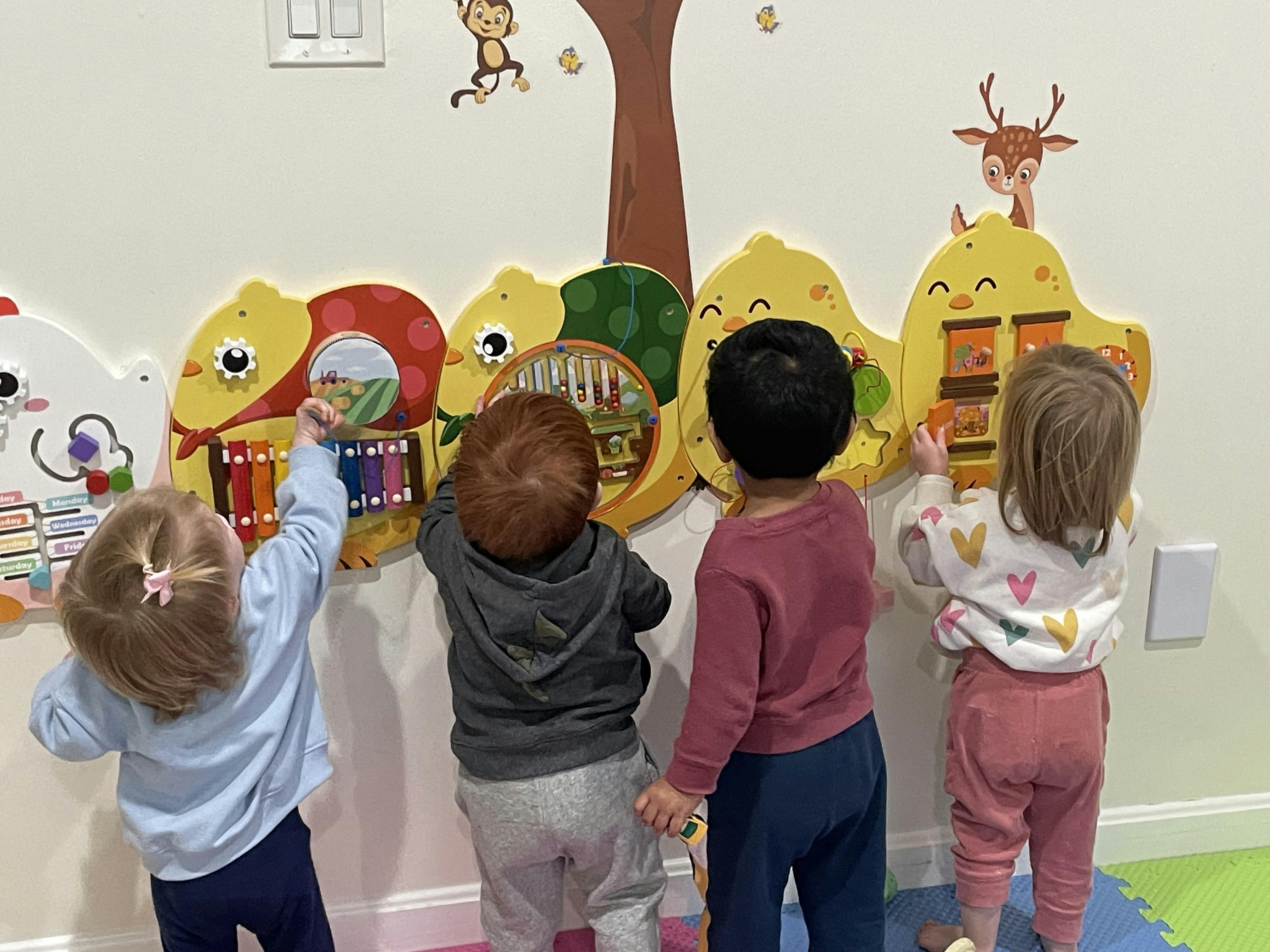 Four children playing with a large wall-mounted activity board
